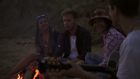 picnic de jóvenes con hoguera en la playa por la noche. amigos alegres cantando canciones y tocando la guitarra. cámara lenta