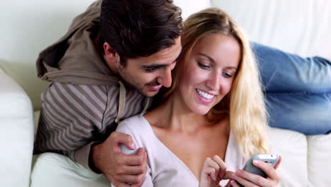 pareja feliz sentada en el sofá mientras la novia está enviando mensajes de texto