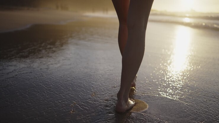 mujer caminando descalza por la playa al atardecer
