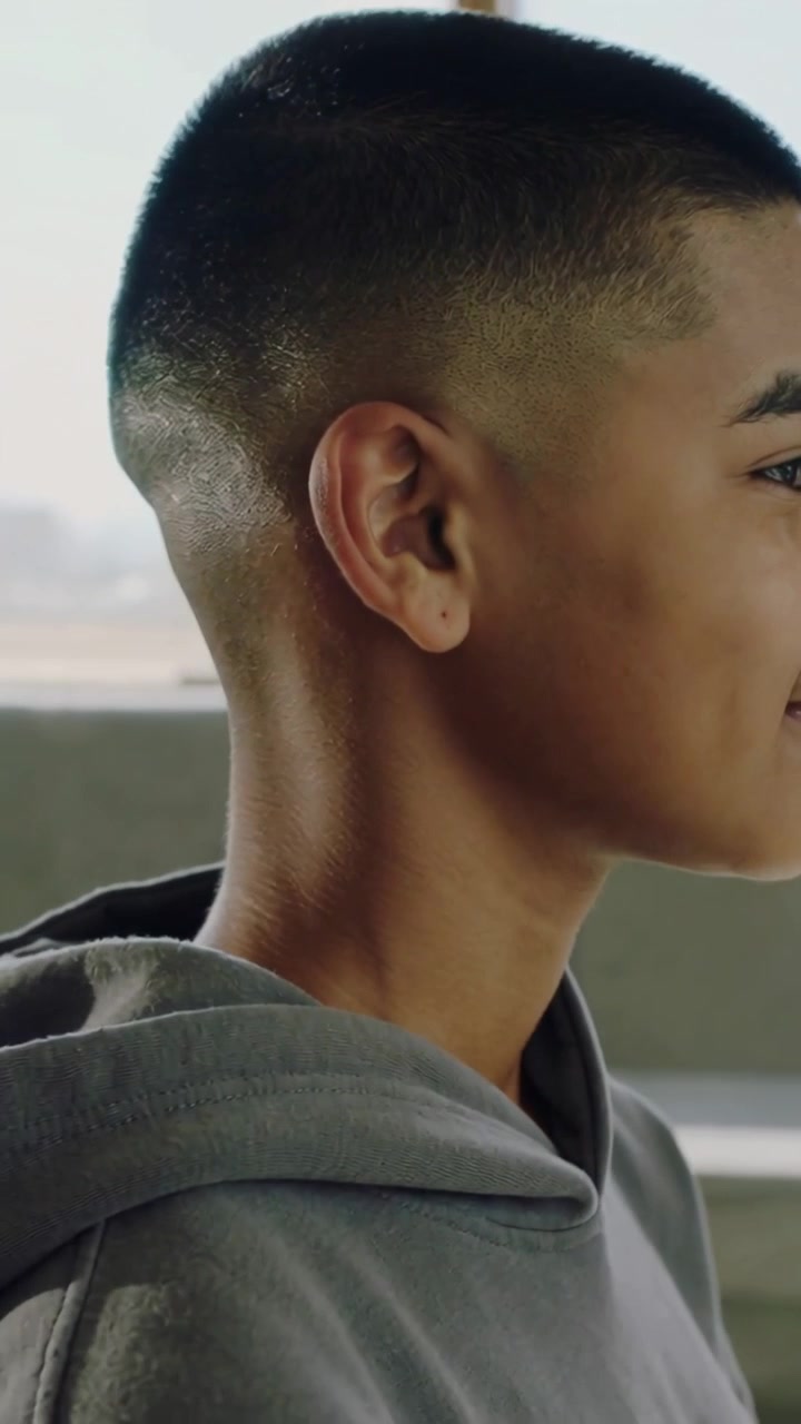 Vertical video: Recording teen turning toward horizon on concrete ledge, grey hoodie, ear stud
