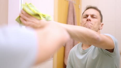 Man cleaning bathroom mirror with spray and cloth