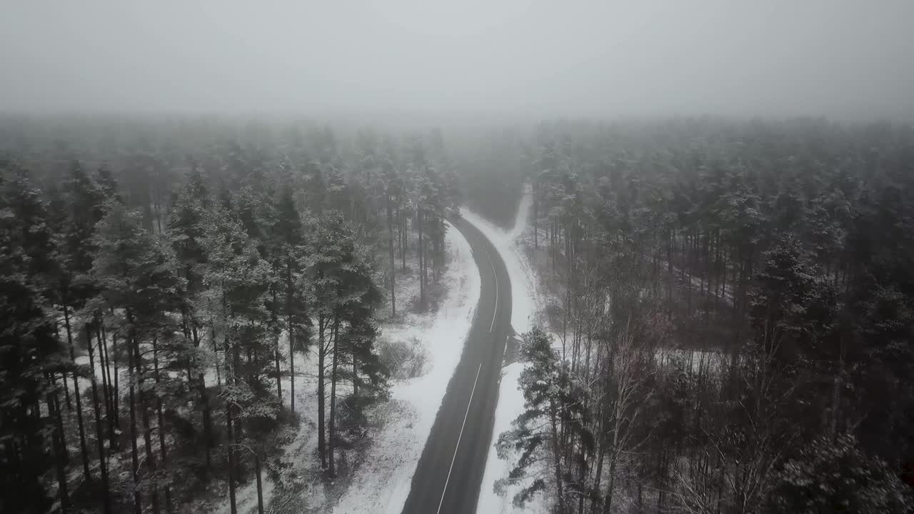 Aerial drone view of empty winter road with forest on both sides and fog