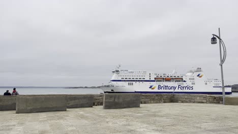 a brittany ferries ship docked in portsmouth on a cloudy day with calm waters.