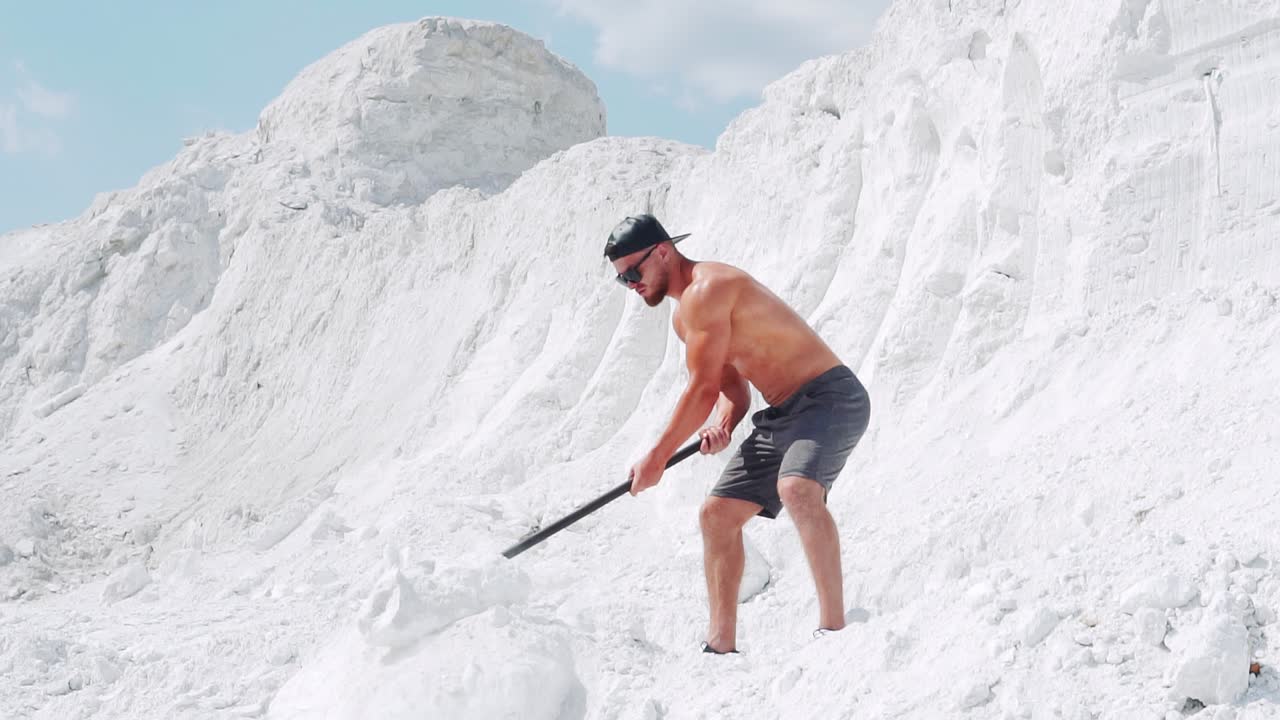 Muscular shirtless man doing exercises with a sledgehammer in a white quarry. Outdoor activities. Slow motion