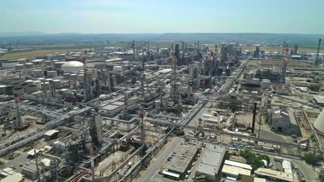 aerial footage of a large scale oil refinery with smoke stacks and petroleum storage tanks