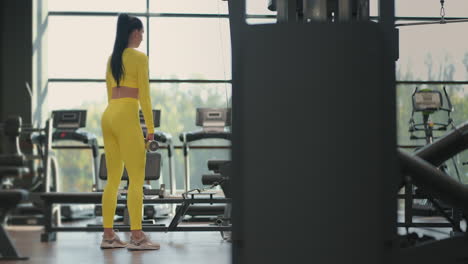 fit hispanic woman performing weight lifting deadlift exercise with dumbbell at gym in yellow sportswear. woman brunette fitness performing doing deadlift exercise with dumbbell