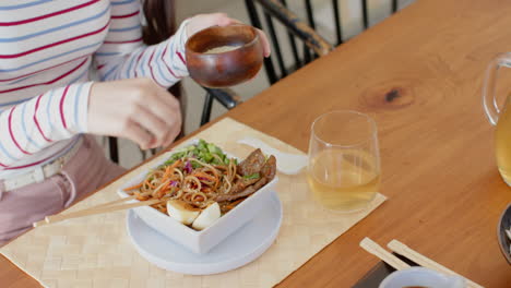 adding seasoning to noodles, woman enjoying meal with drink at dining table