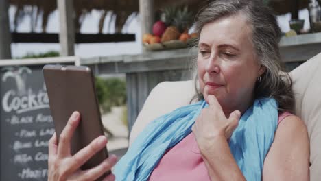 Happy-senior-caucasian-woman-sitting-in-hammock-using-smartphone-by-beach-bar,-in-slow-motion