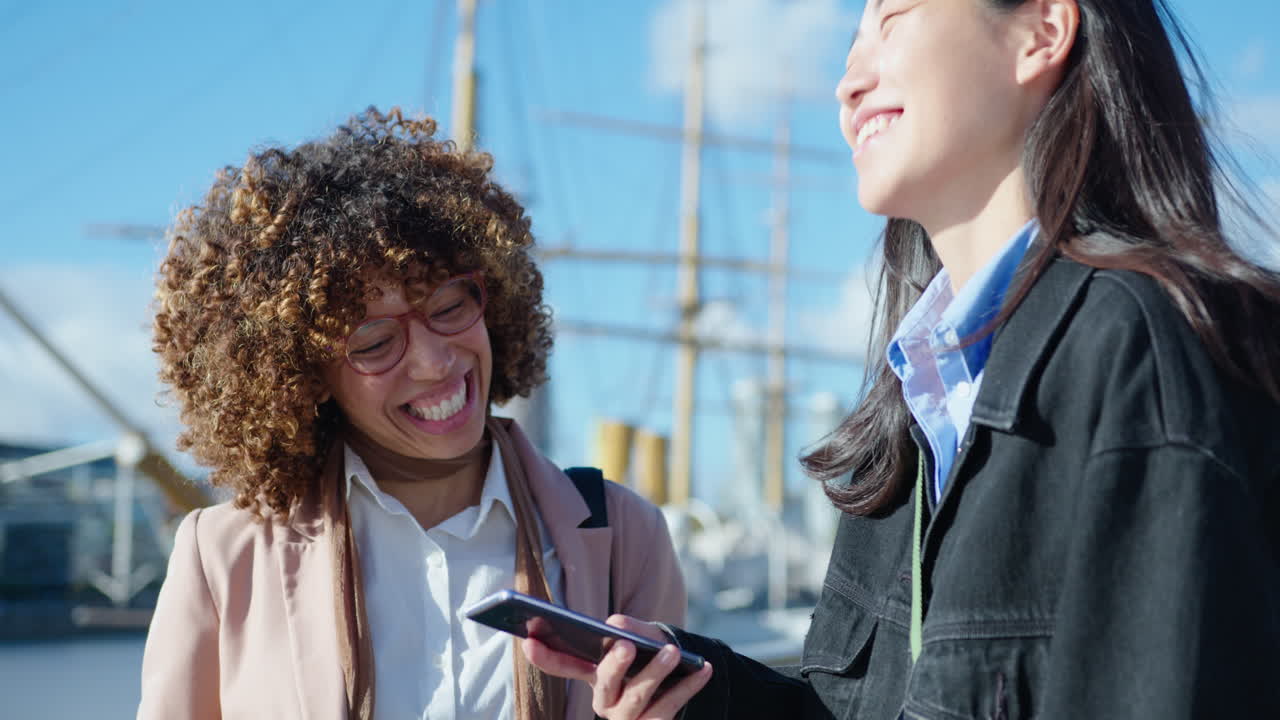 Cheerful Female Colleagues Using Smartphone and Chatting Outdoors in the City