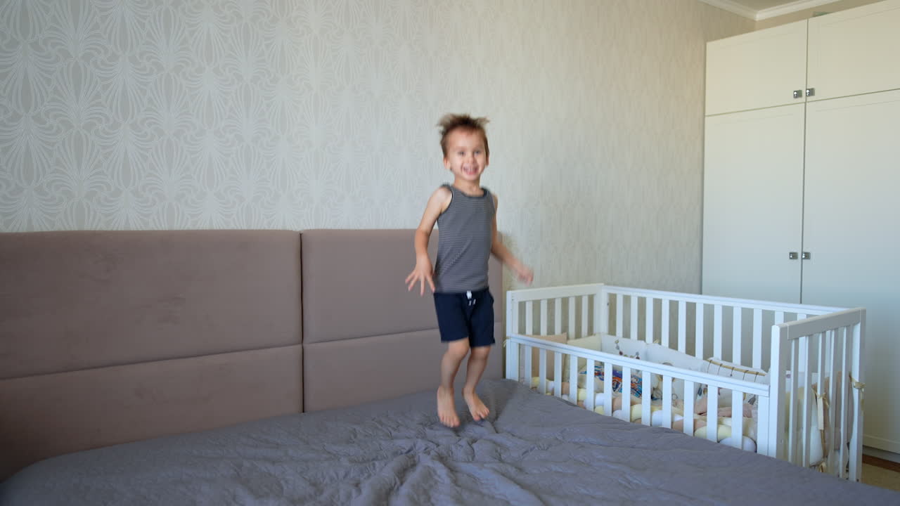 Happy toddler boy jumps on the big double bed. Healthy active energetic child at home.