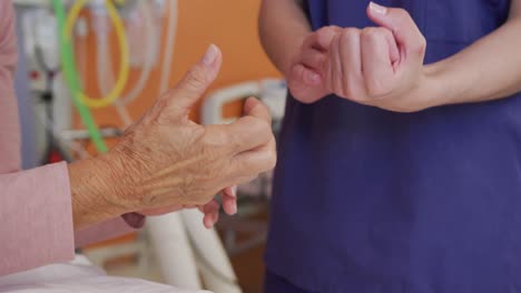 doctora biracial examinando la mano de una paciente caucásica anciana en el hospital