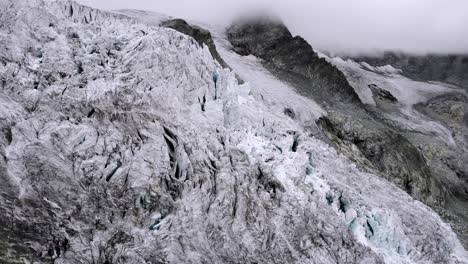 aerial flyover over a hiker at a viewpoint of the moiry glacier near grimentz in valais, switzerland with a view of the icy crevasses as mountains hide in the clouds