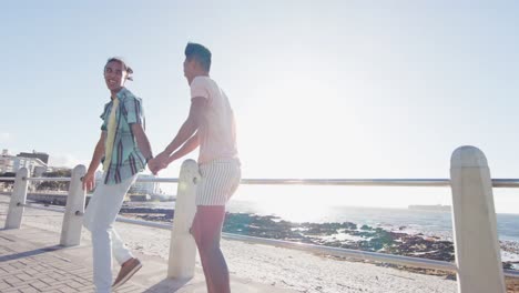 Happy-diverse-gay-male-couple-walking-and-holding-hands-at-promenade-by-the-sea,-slow-motion