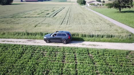 볼보 xc 90suv 자동차는 두 도로, 스위스 시골, 보드, 무인 항공기 추적 공중 보기 사이의 교차로 후 농업 분야 사이의 작은 울퉁불퉁한 도로에서 천천히 운전합니다.