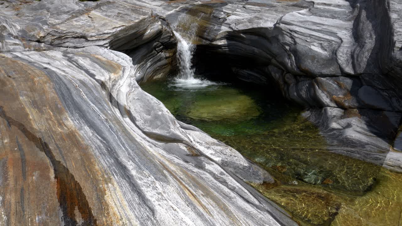 Beautiful creek water cascades carving shallow pool with washed stones
