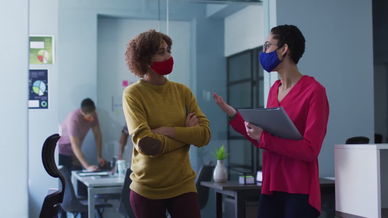 Mixed race female colleagues wearing face masks in office