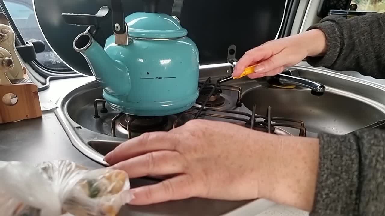 Female hand ignites gas cooker hob in campervan kitchen to boil vintage steam kettle water
