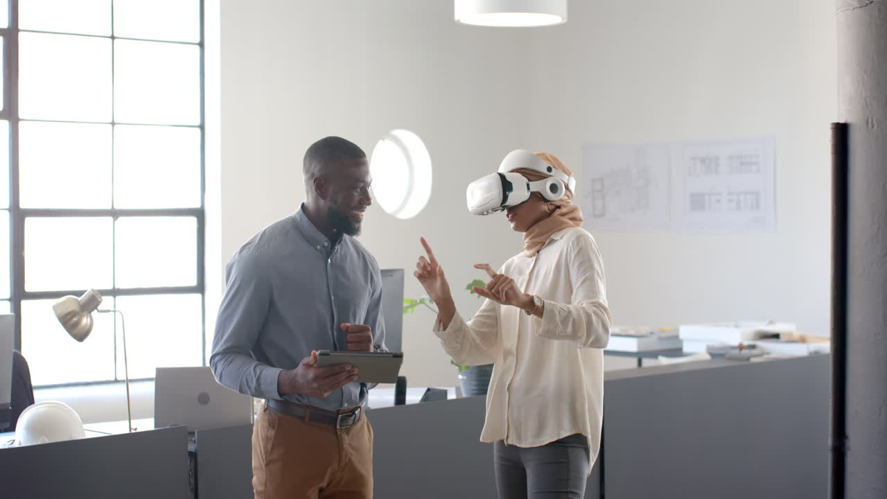 Kvinde bruger VR-headset og diskuterer projekt med kollega, der holder tablet, på kontoret.