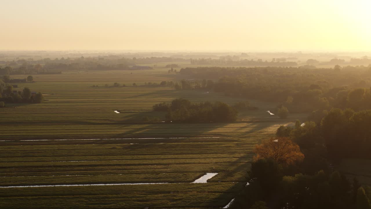 Drone shot of green and wet Dutch landscape as the sun sets on the horizon