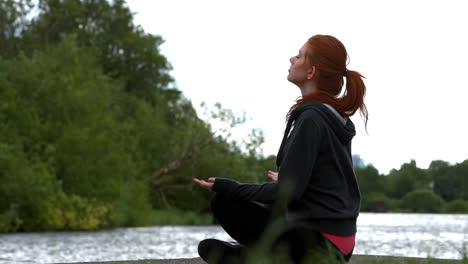 pelirroja tranquila haciendo yoga junto a un lago