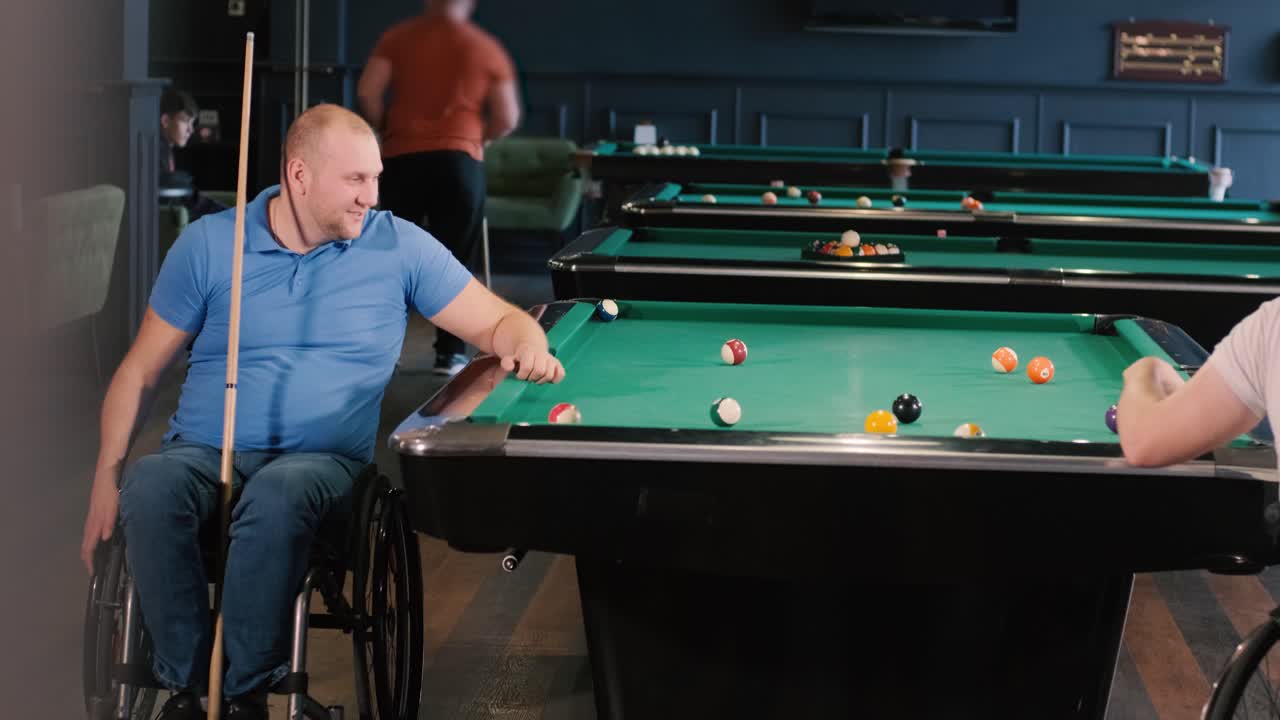 Adult men with disabilities in a wheelchair play billiards in the club