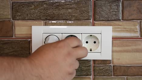 la mano de un hombre conectando y desconectando varios dispositivos domésticos a un enchufe de pared triple