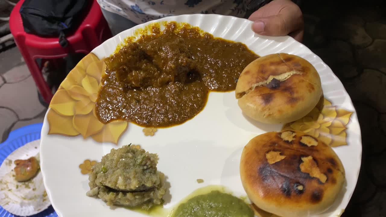 hombre que sostiene un plato de litti chokha que incluye 2 litti, delicioso baigan bharta, chutney verde picante y curry de cordero