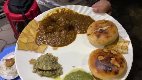 man holding a plate of litti chokha which includes 2 litti, delicious baigan bharta, spicy green chutney and mutton curry