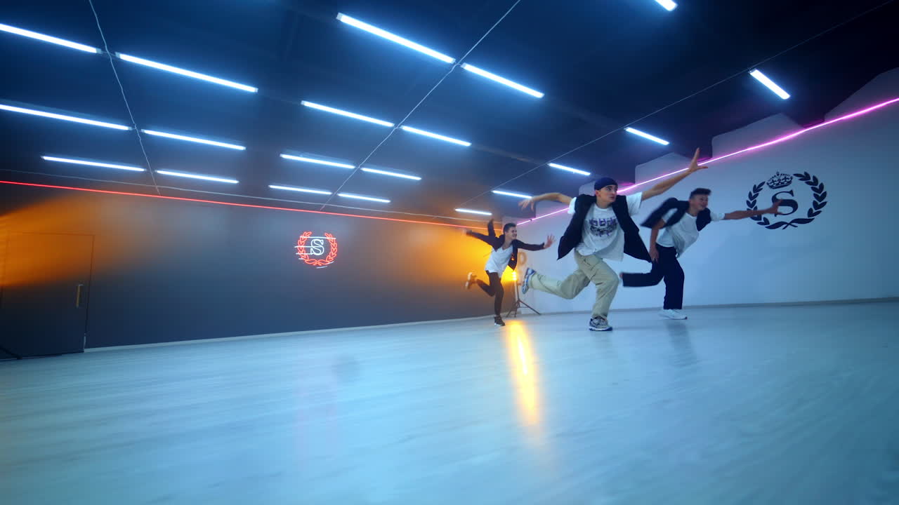 Three male dancers showing a dance in the spacious studio. Boys band dancing hip hop. Low angle view.