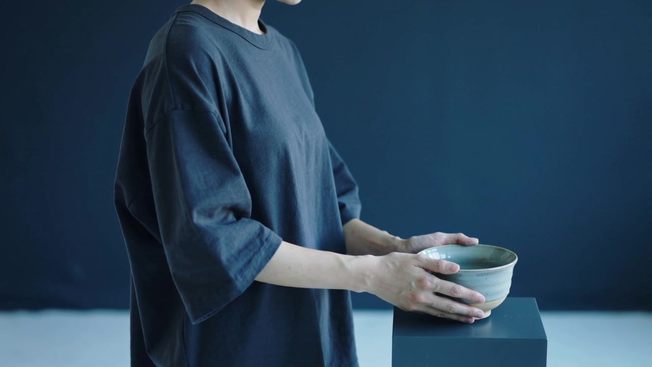 Donna con maglietta scura che tiene una ciotola e la posiziona su un piedistallo per l'esposizione in studio