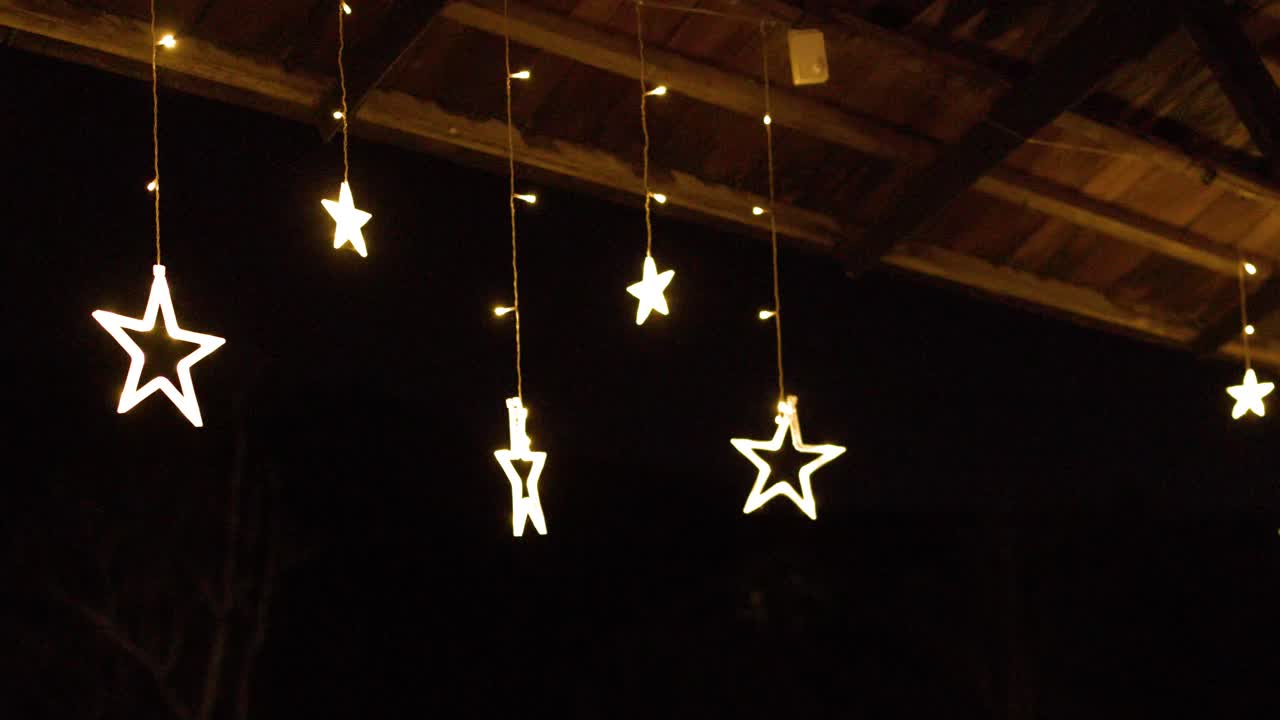 Warm star shaped string lights hang from a dark wooden terrace ceiling at night