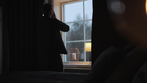 desperate upset man looks outside window from bedroom covering his face, static