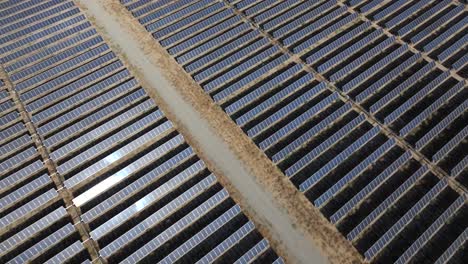 An-aerial-view-of-a-solar-farm-with-endless-rows-of-solar-panels,-with-the-sun's-reflection