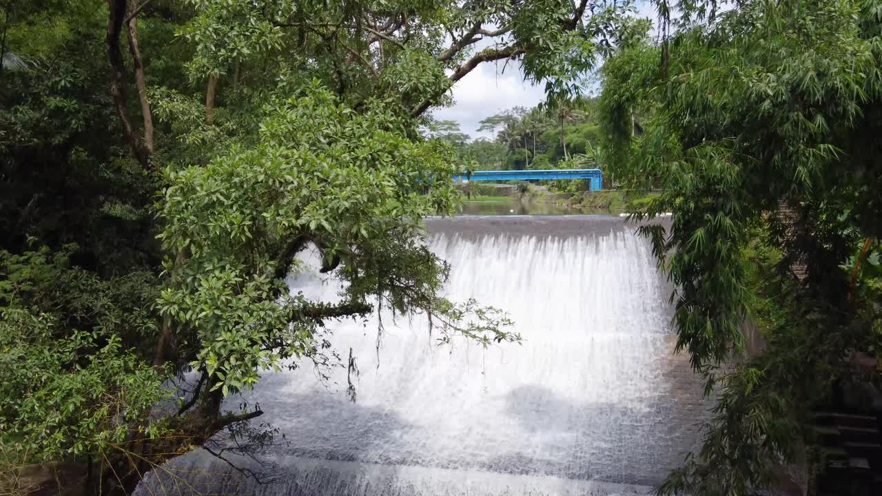 Aerial : Air Terjun Bandung waterfall : river water flowing down an old historic dam in a tropical Jungle Bali, Ubud &ndash; Indonesia