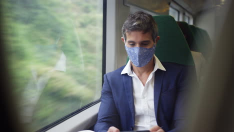 businessman on train using mobile phone wearing ppe face mask during health pandemic