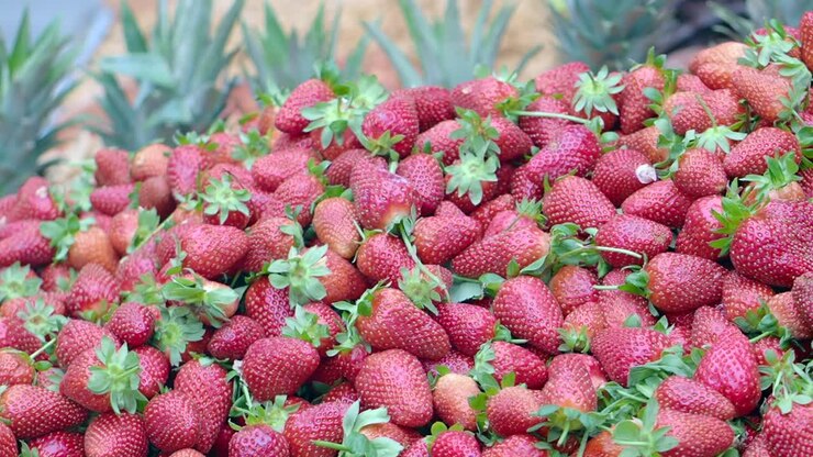 Pile of fresh strawberries with pineapple tops in the background