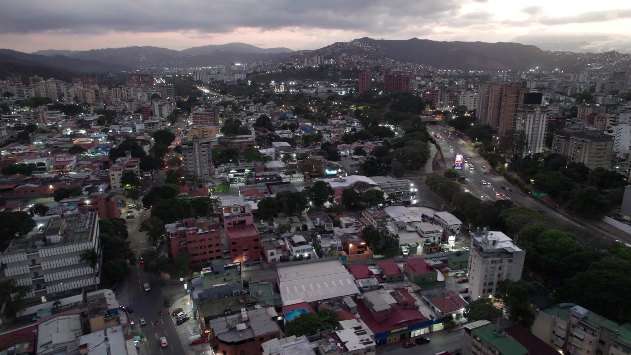 Vista panoramica dall'alto di auto che percorrono l'autostrada cittadina accanto a una zona residenziale al tramonto a Caracas
