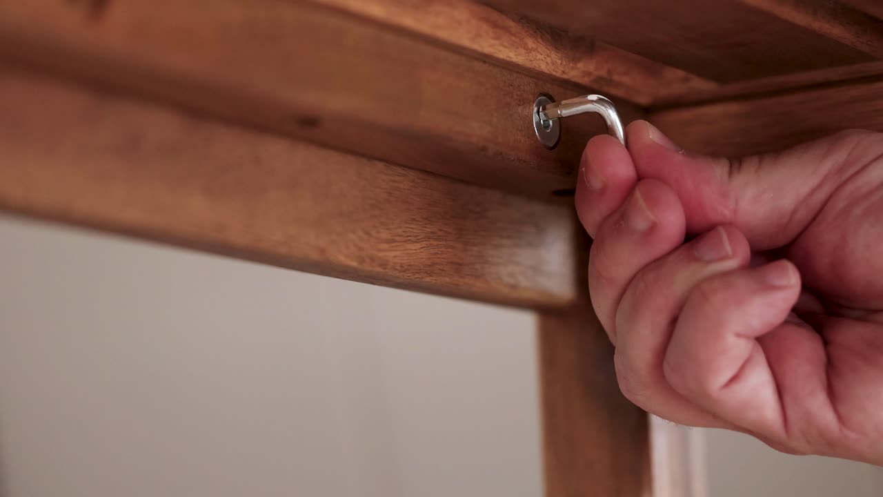 Hands tighten screws on wooden furniture using an Allen key. Close-up shots highlight precision and craftsmanship