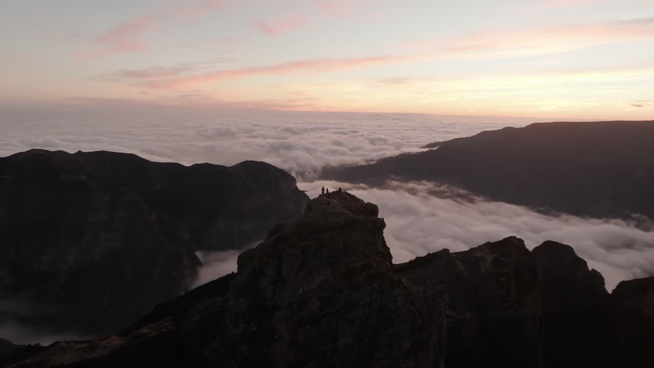 Drone che orbita un affioramento roccioso sopra nuvole dense all'alba a Pico do Arieiro, Madeira, con persone in piedi sulla cima.