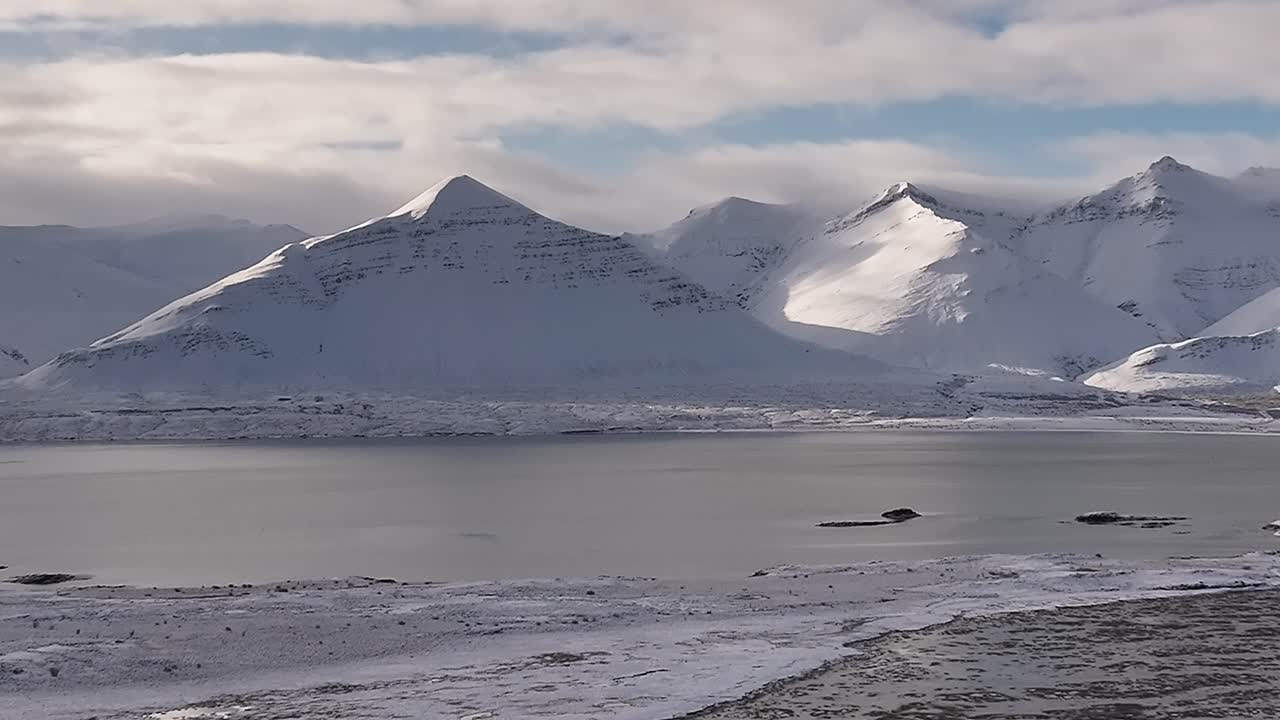 Aerial zoom-in over snowy Borgarfjörður bay with dramatic peaks in the background, Iceland.