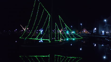 drone approaches galway hooker boats with string lights as sails at night over open water