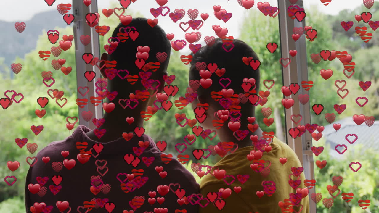 Two men standing by sliding door, watching garden while showing animated red hearts in tech demo