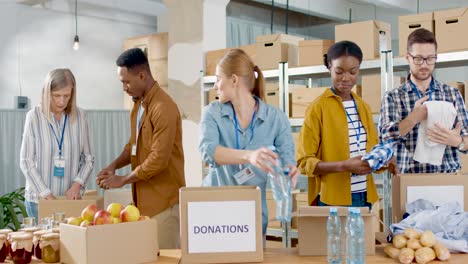 multiethnic group of volunteers packing boxes with food and clothes in charity warehouse