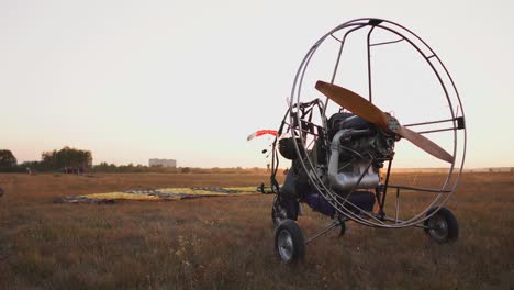 el parapente de motor se encuentra en el aeropuerto en los rayos de la luz del atardecer. en el fondo, un paracaidista aterriza y la cámara se mueve lentamente alrededor del parapente