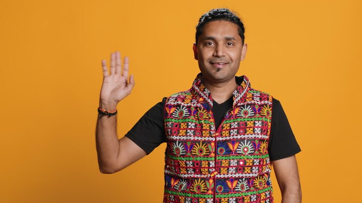 Ritratto di uomo allegro che sorride e saluta con la mano, sfondo in studio