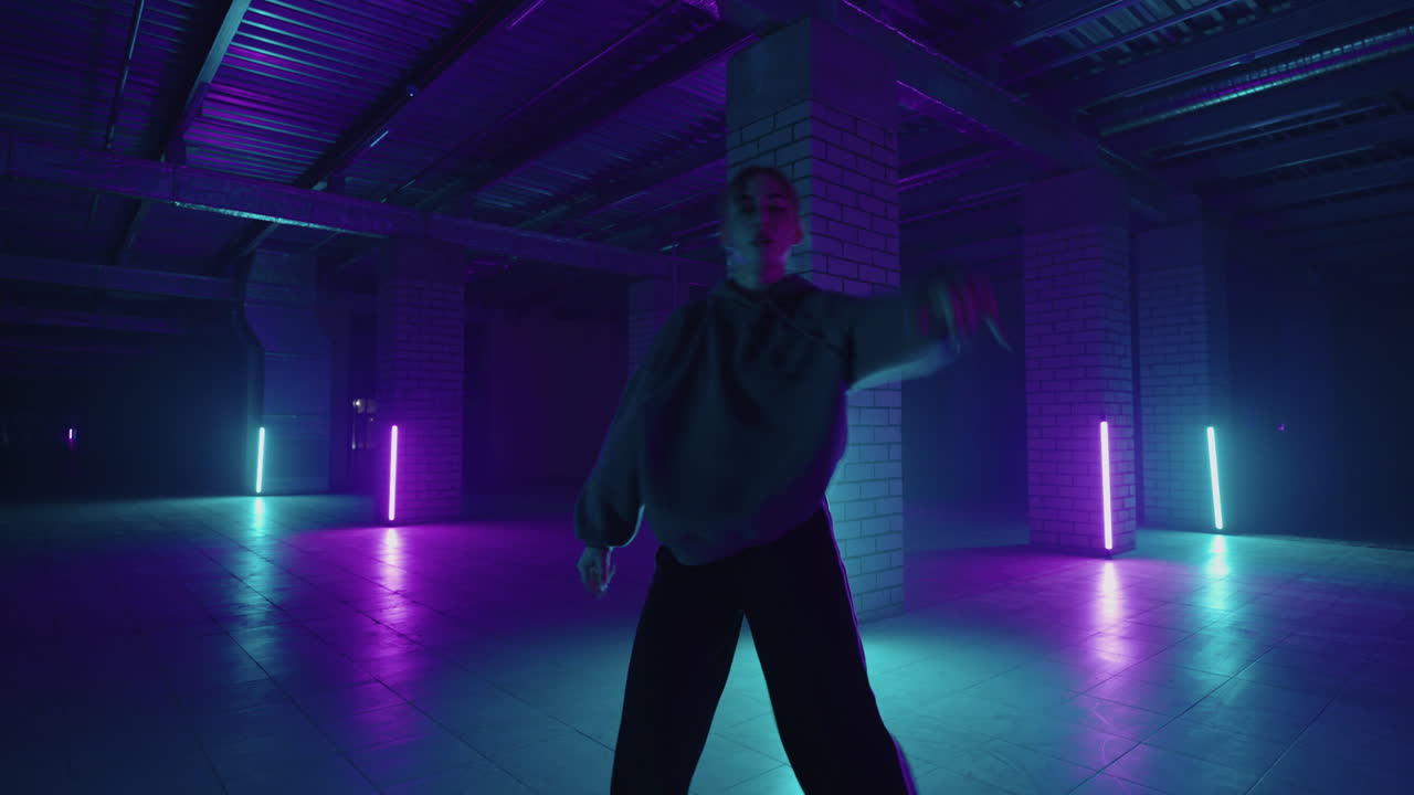 bailarina elegante se mueve a la música en una habitación llena de humo con iluminación de neón. mujer dando una actuación en solitario en estilo hip hop en la escena del club con lámparas de neón de fondo