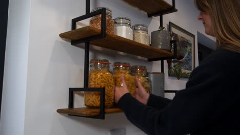 female model choosing then taking a jar of pasta from kitchen shelves in a kitchen