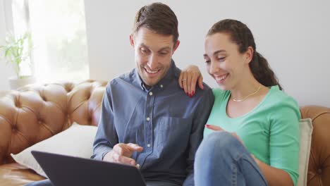una joven pareja caucásica hablando y pagando sus cuentas usando una computadora portátil