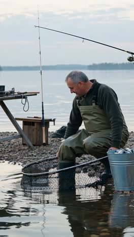 man fishing by a lake with a net and bucket