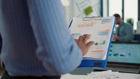 closeup of african american woman hands holding clipboard with financial data and sales charts